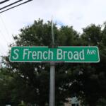 Green street sign reading "S French Broad Ave" with trees and power lines in the background.