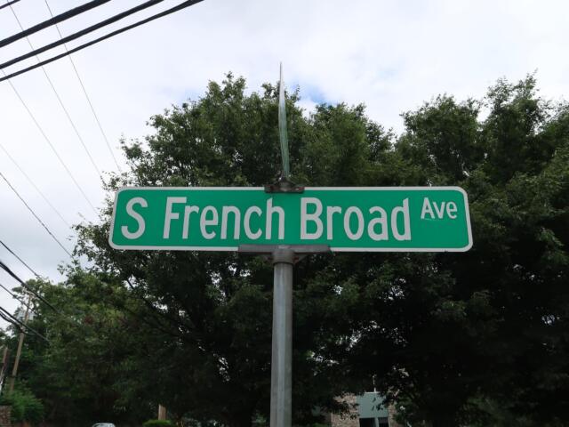 Green street sign reading "S French Broad Ave" with trees and power lines in the background.