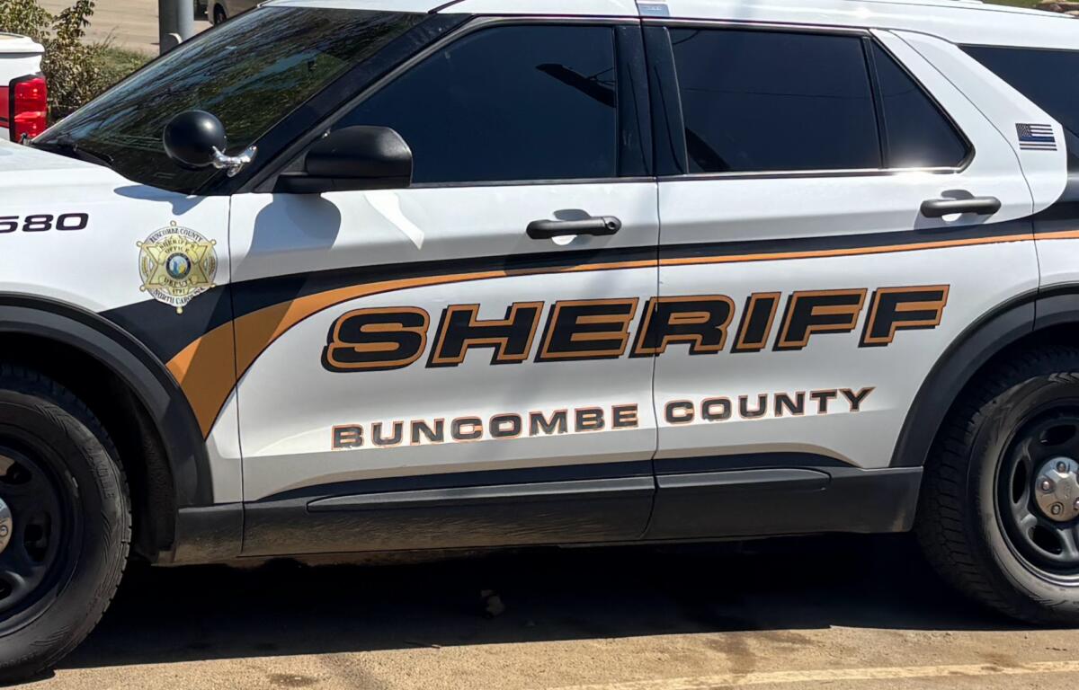 White sheriff SUV with orange/black graphics reading Buncombe County Sheriff; badge emblem on front door.