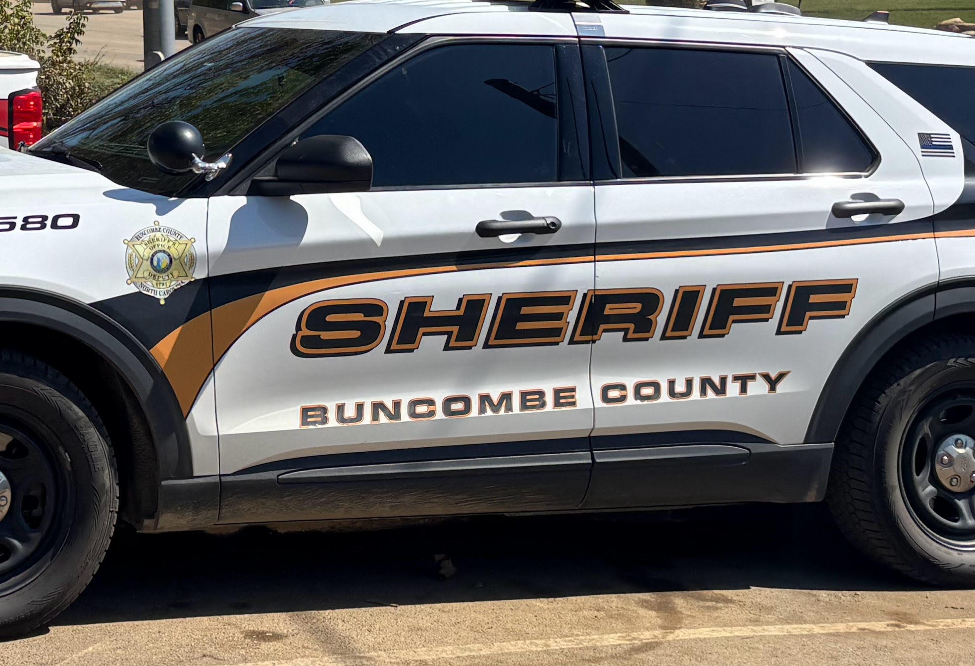 White sheriff SUV with orange/black graphics reading Buncombe County Sheriff; badge emblem on front door.