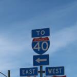 Blue highway sign cluster: 'TO' above a red-arched Interstate 40 shield with large 40, arrows pointing left for directions (east/west signs visible) on a clear sky backdrop.