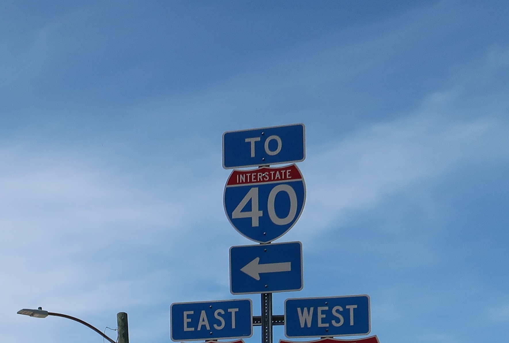 Blue highway sign cluster: 'TO' above a red-arched Interstate 40 shield with large 40, arrows pointing left for directions (east/west signs visible) on a clear sky backdrop.