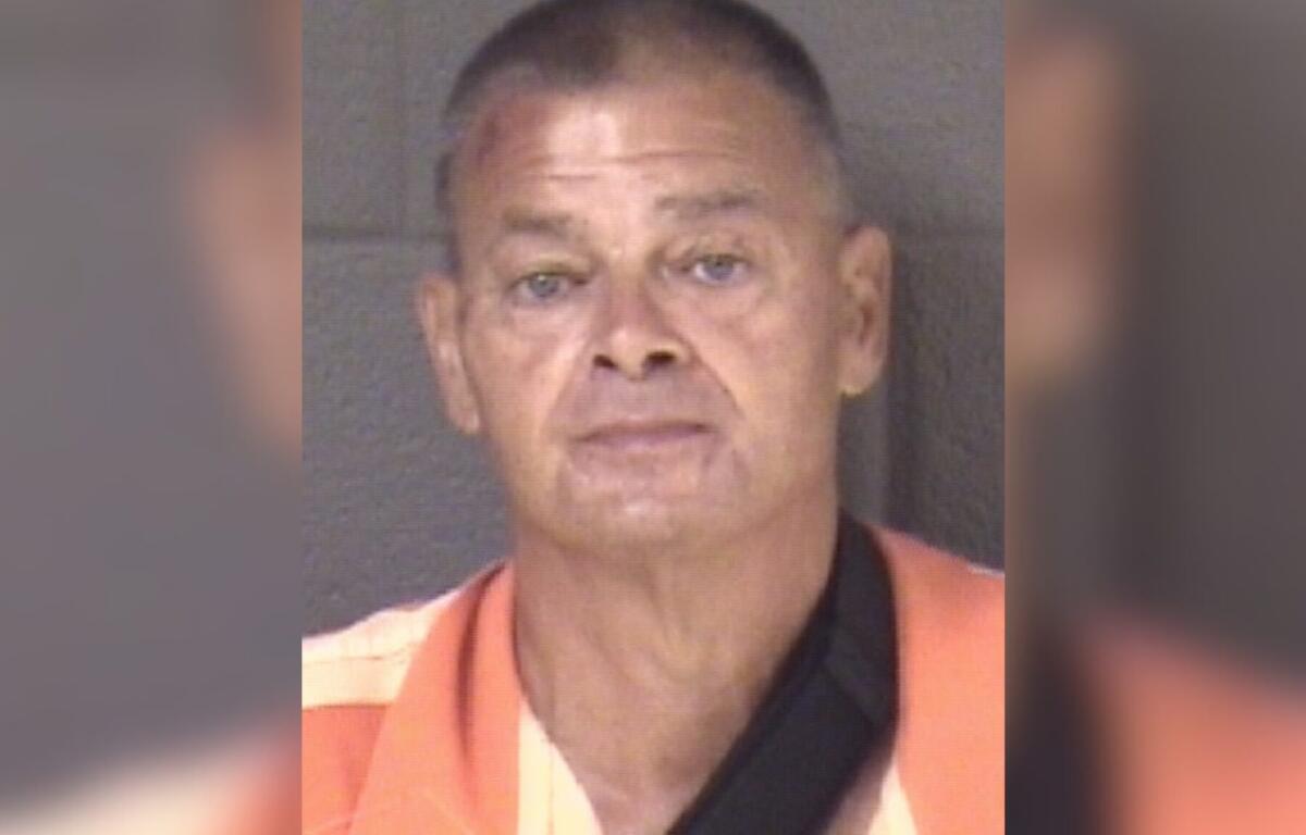 Mugshot of a middle-aged man with short hair wearing an orange prison jumpsuit, facing the camera against a gray backdrop.