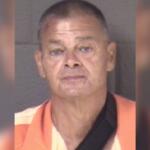 Mugshot of a middle-aged man with short hair wearing an orange prison jumpsuit, facing the camera against a gray backdrop.