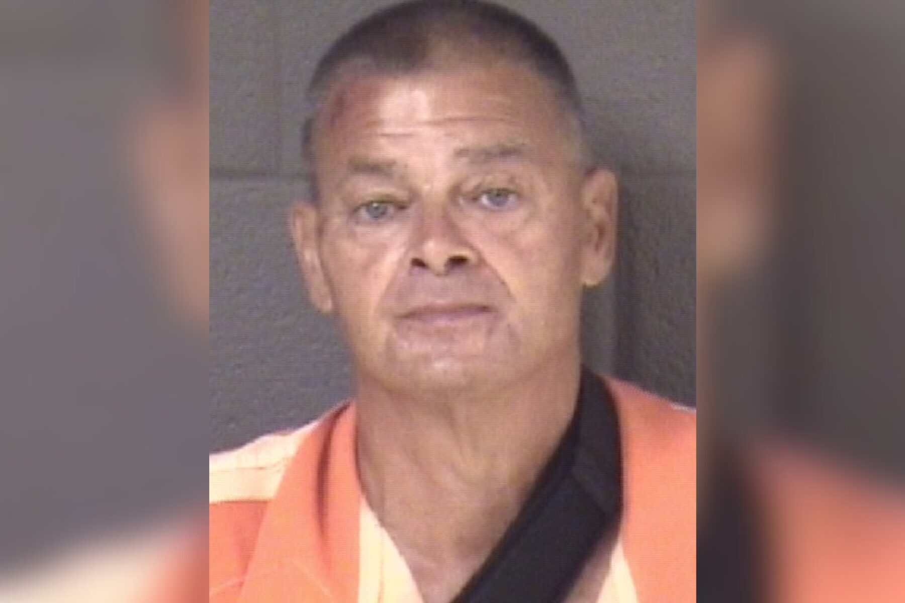 Mugshot of a middle-aged man with short hair wearing an orange prison jumpsuit, facing the camera against a gray backdrop.