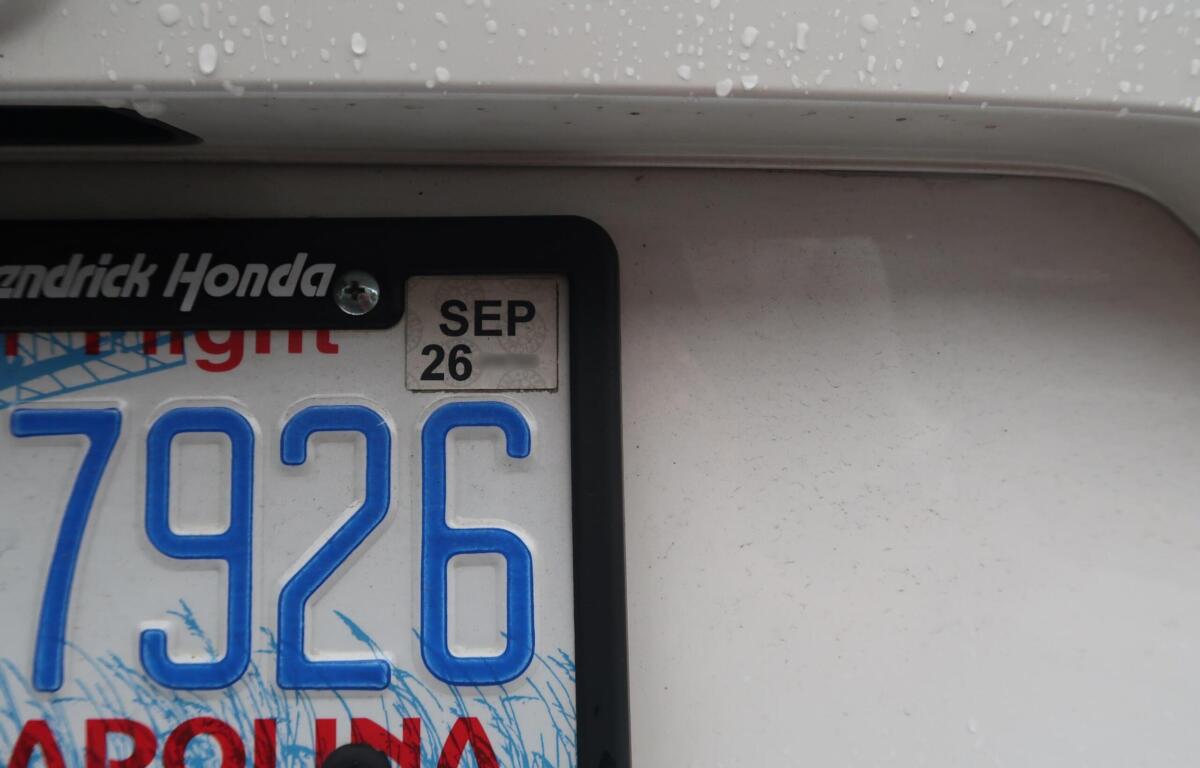 Close-up of a car license plate frame reading 'Hendrick Honda' with a SEP 26 sticker and blue numbers, raindrops on the car surface.