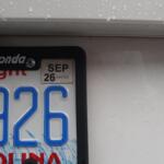 Close-up of a car license plate frame reading 'Hendrick Honda' with a SEP 26 sticker and blue numbers, raindrops on the car surface.