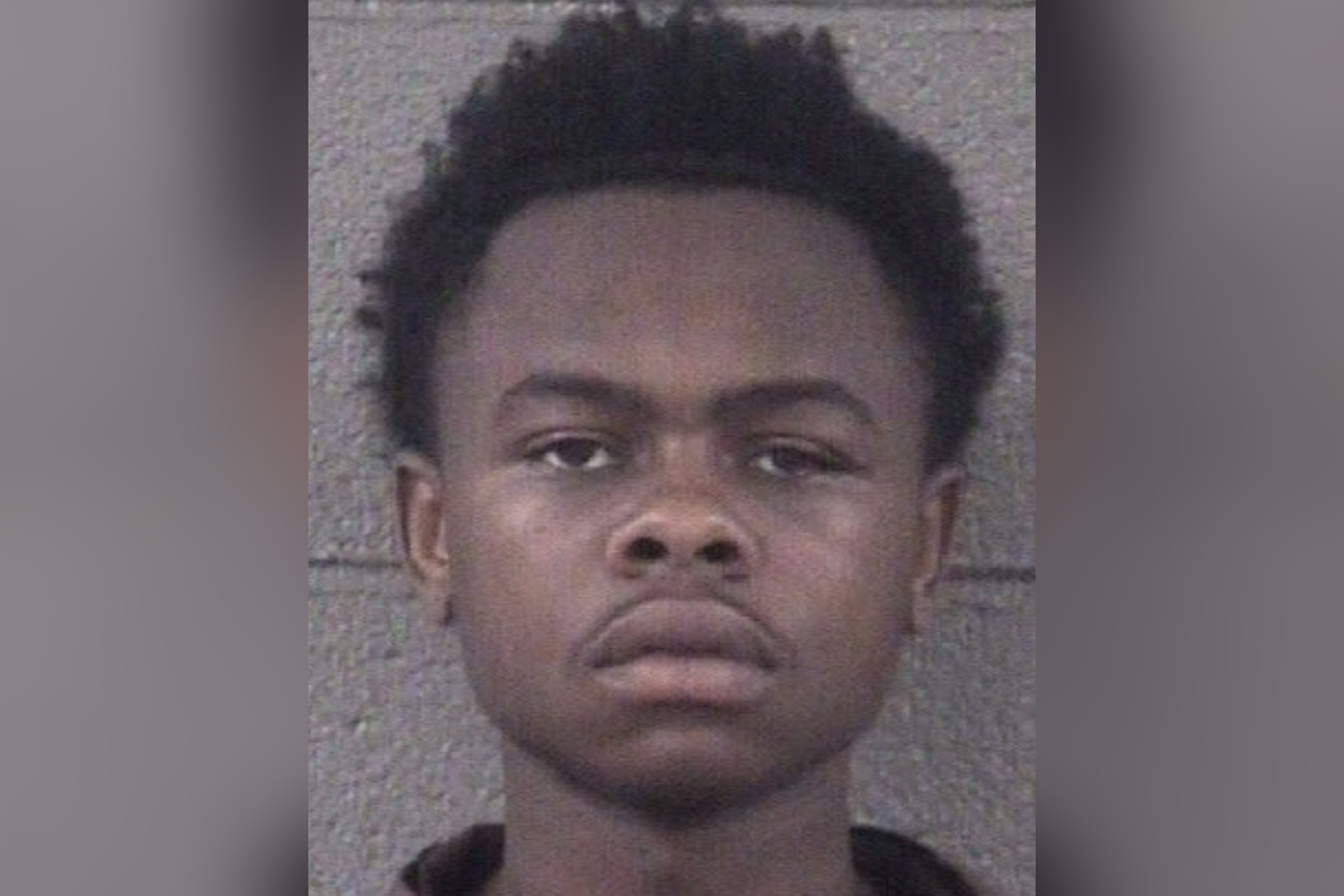 Mugshot photo of a young Black man facing the camera with a neutral expression, against a gray background.