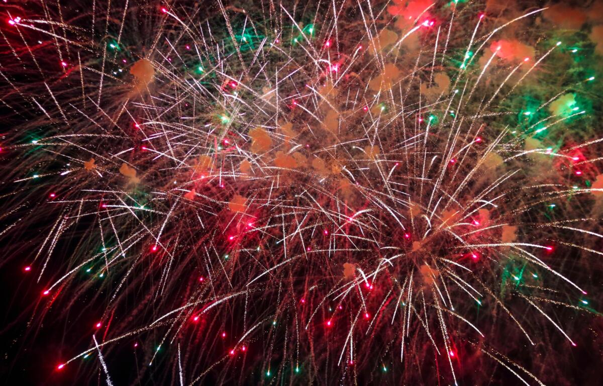 Fireworks explode in a dark sky, white streaks crisscrossing with red and green sparks and smoke.