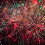 Fireworks explode in a dark sky, white streaks crisscrossing with red and green sparks and smoke.