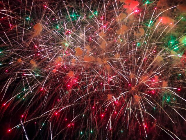 Fireworks explode in a dark sky, white streaks crisscrossing with red and green sparks and smoke.