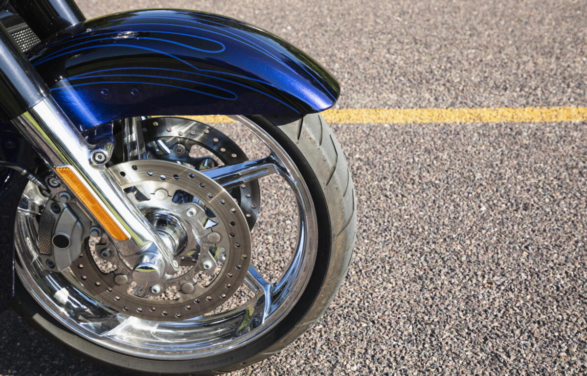 Close-up of a blue motorcycle front fender with decorative pinstripes, chrome forks, and a perforated brake disc.