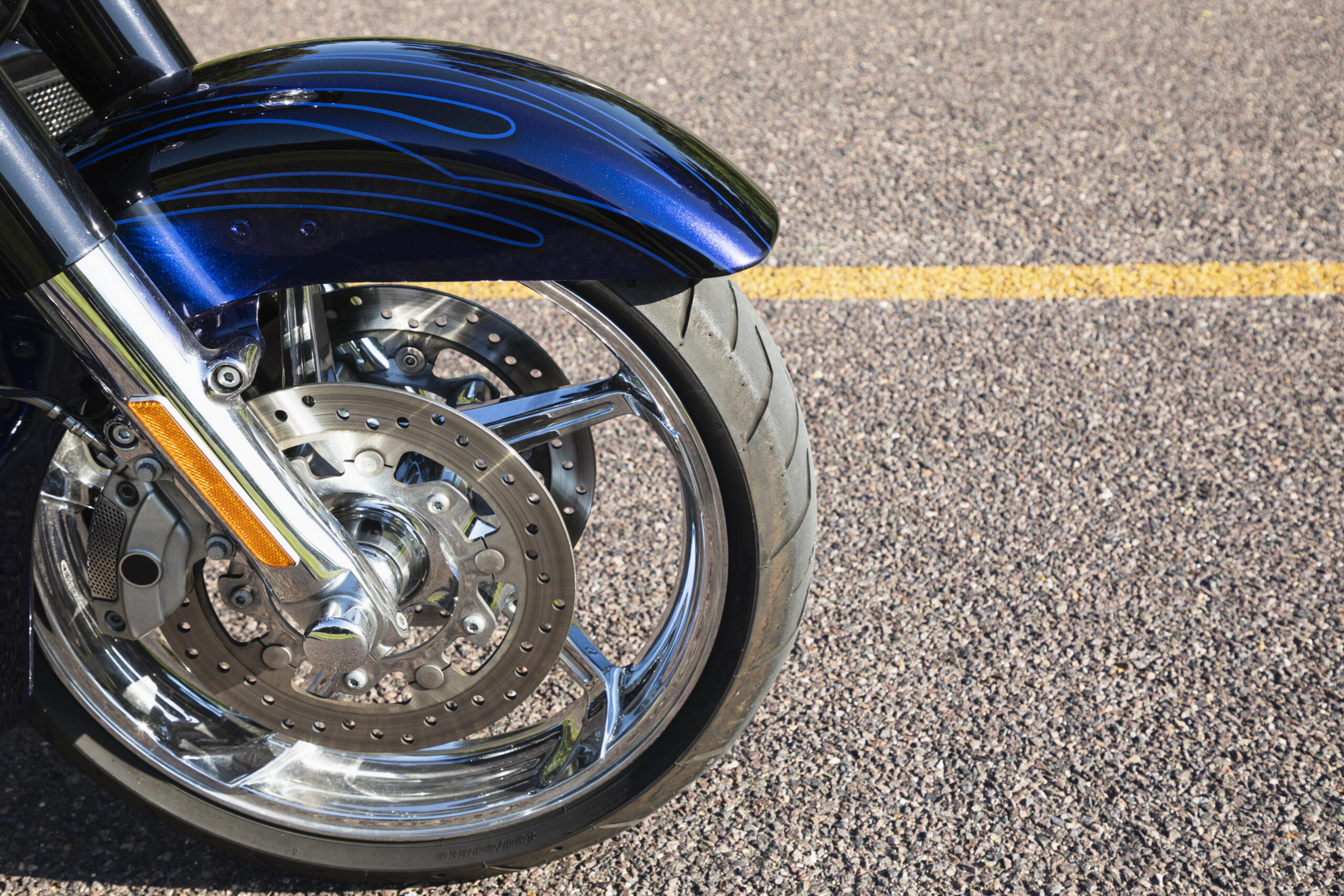 Close-up of a blue motorcycle front fender with decorative pinstripes, chrome forks, and a perforated brake disc.