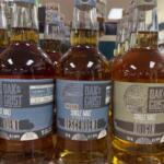 Three Oak Grist single malt whiskeys on a store shelf, labels show Descendent and Original variants.