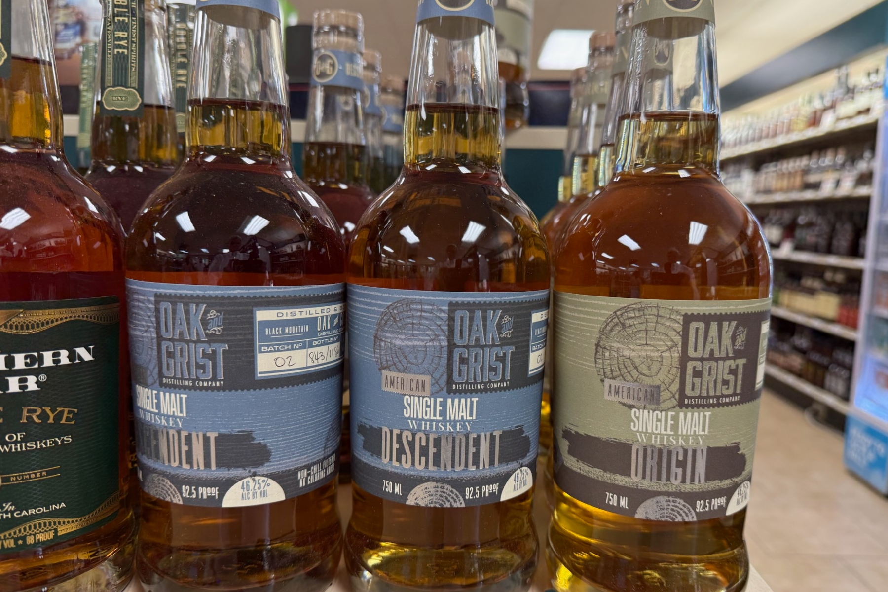 Three Oak Grist single malt whiskeys on a store shelf, labels show Descendent and Original variants.