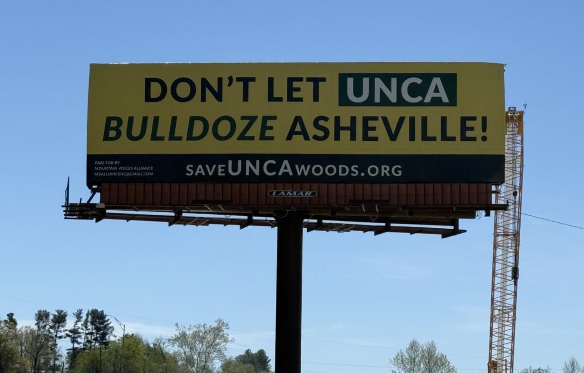 A "Save the Woods" billboard stands along Future I-26 in Asheville, highlighting community opposition to potential development of UNC Asheville's South Campus woods.