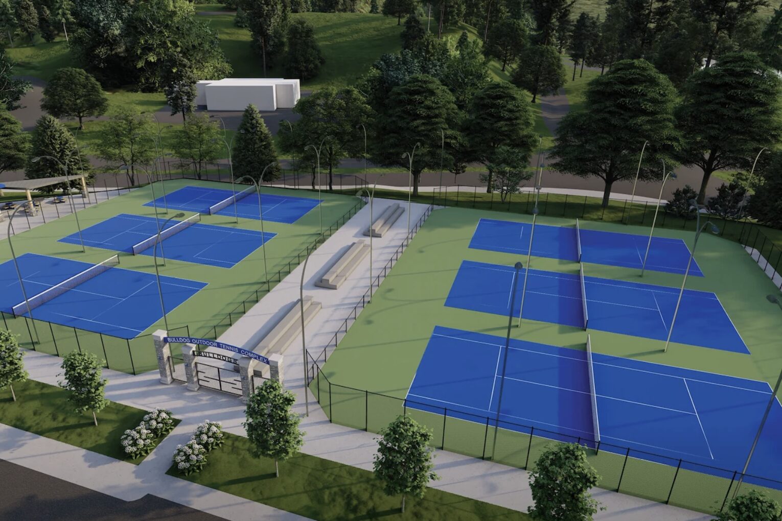 Aerial view of a tennis complex with several blue courts, green fencing, and surrounding trees in a park-like setting.