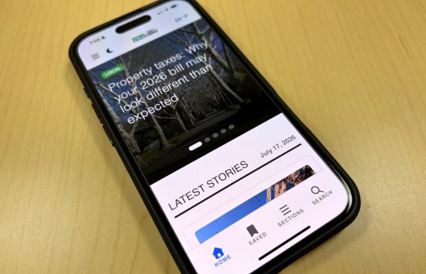 Smartphone displaying a news app with a headline about property taxes on a wooden table surface