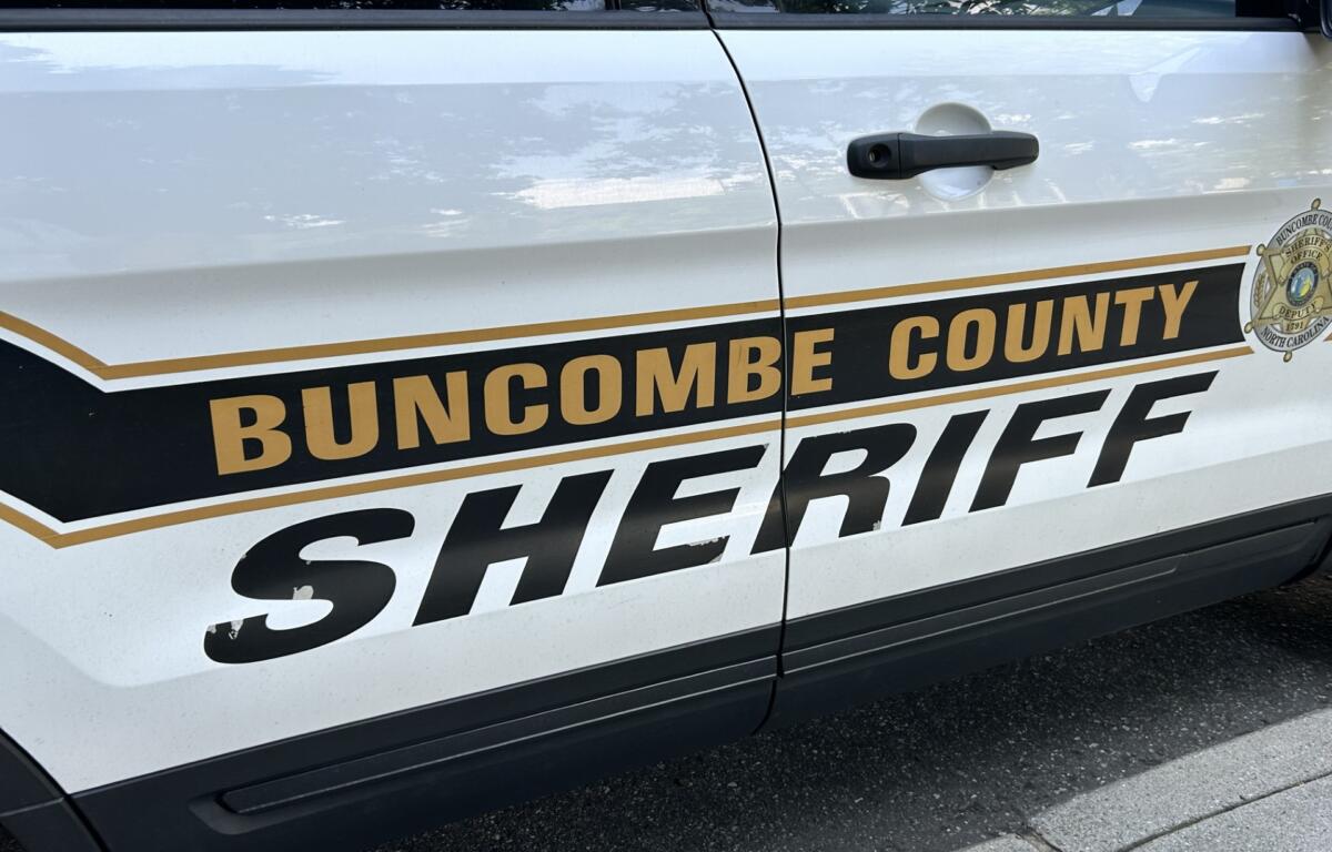 White Buncombe County Sheriff's Office patrol vehicle door with gold and black 'SHERIFF' lettering and sheriff badge visible on the side