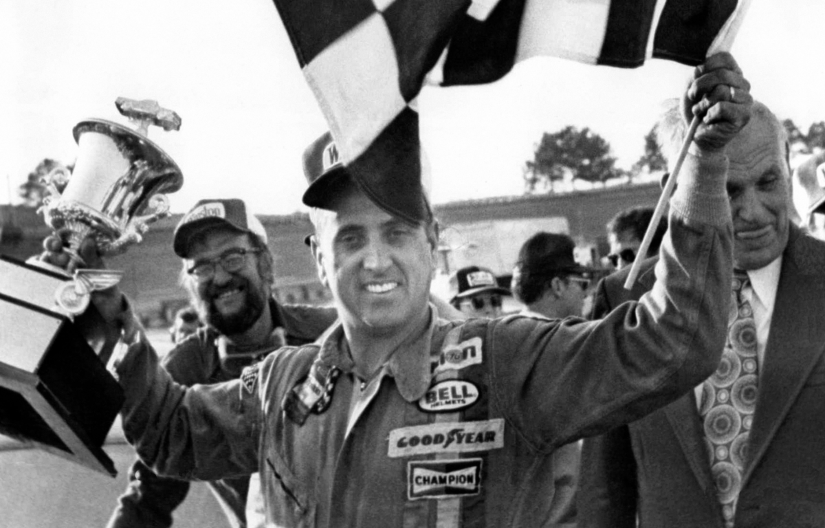 FILE - In this Nov. 8, 1976, file photo, stock car driver David Marcis waves a checkered flag and hold his winner's trophy after the Dixie 500 in Hampton, Ga. Only 39 cars showed up for the second race of the Sprint Cup season, the lowest number of entries in more than two decades. While the reduced numbers won't affect front-runners such as Daytona 500 winner Denny Hamlin _ after all, we're talking about low-budget drivers who probably would've been lapped early in the race _ it does drive home the end of an era. "We've lost a lot," said former driver Dave Marcis, who spent much of his long career simply trying to qualify for races in under-financed cars. (AP Photo/Lennox McLendon, File)