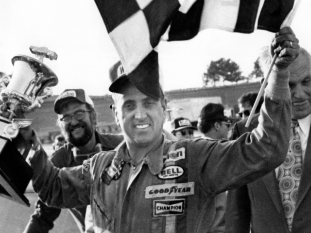 FILE - In this Nov. 8, 1976, file photo, stock car driver David Marcis waves a checkered flag and hold his winner's trophy after the Dixie 500 in Hampton, Ga. Only 39 cars showed up for the second race of the Sprint Cup season, the lowest number of entries in more than two decades. While the reduced numbers won't affect front-runners such as Daytona 500 winner Denny Hamlin _ after all, we're talking about low-budget drivers who probably would've been lapped early in the race _ it does drive home the end of an era. "We've lost a lot," said former driver Dave Marcis, who spent much of his long career simply trying to qualify for races in under-financed cars. (AP Photo/Lennox McLendon, File)