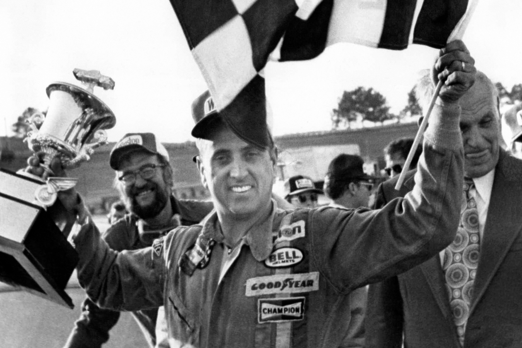 FILE - In this Nov. 8, 1976, file photo, stock car driver David Marcis waves a checkered flag and hold his winner's trophy after the Dixie 500 in Hampton, Ga. Only 39 cars showed up for the second race of the Sprint Cup season, the lowest number of entries in more than two decades. While the reduced numbers won't affect front-runners such as Daytona 500 winner Denny Hamlin _ after all, we're talking about low-budget drivers who probably would've been lapped early in the race _ it does drive home the end of an era. "We've lost a lot," said former driver Dave Marcis, who spent much of his long career simply trying to qualify for races in under-financed cars. (AP Photo/Lennox McLendon, File)
