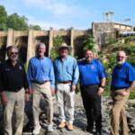 From left: Polk County Commission Chairman Myron Yoder, DEQ Secretary Reid Wilson, DEMLR Director Toby Vinson, Polk County Emergency Management Director Bobby Arledge and Polk County Manager Marche Pittman pose in front of the Turner Shoals Dam, which received $1.3 million to repair damage from Hurricane Helene.