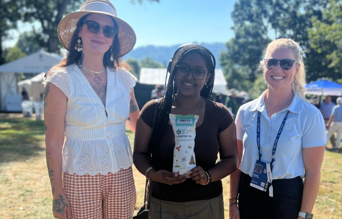 Asheville High School art teacher Kristina Shriver, left, and student Nia Teshome pose with a PGA TOUR representative during the Biltmore Championship Asheville. Teshome holds one of the limited-edition Poppy Hand-Crafted Popcorn bags featuring artwork created by Asheville High students.