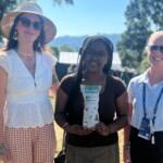 Asheville High School art teacher Kristina Shriver, left, and student Nia Teshome pose with a PGA TOUR representative during the Biltmore Championship Asheville. Teshome holds one of the limited-edition Poppy Hand-Crafted Popcorn bags featuring artwork created by Asheville High students.