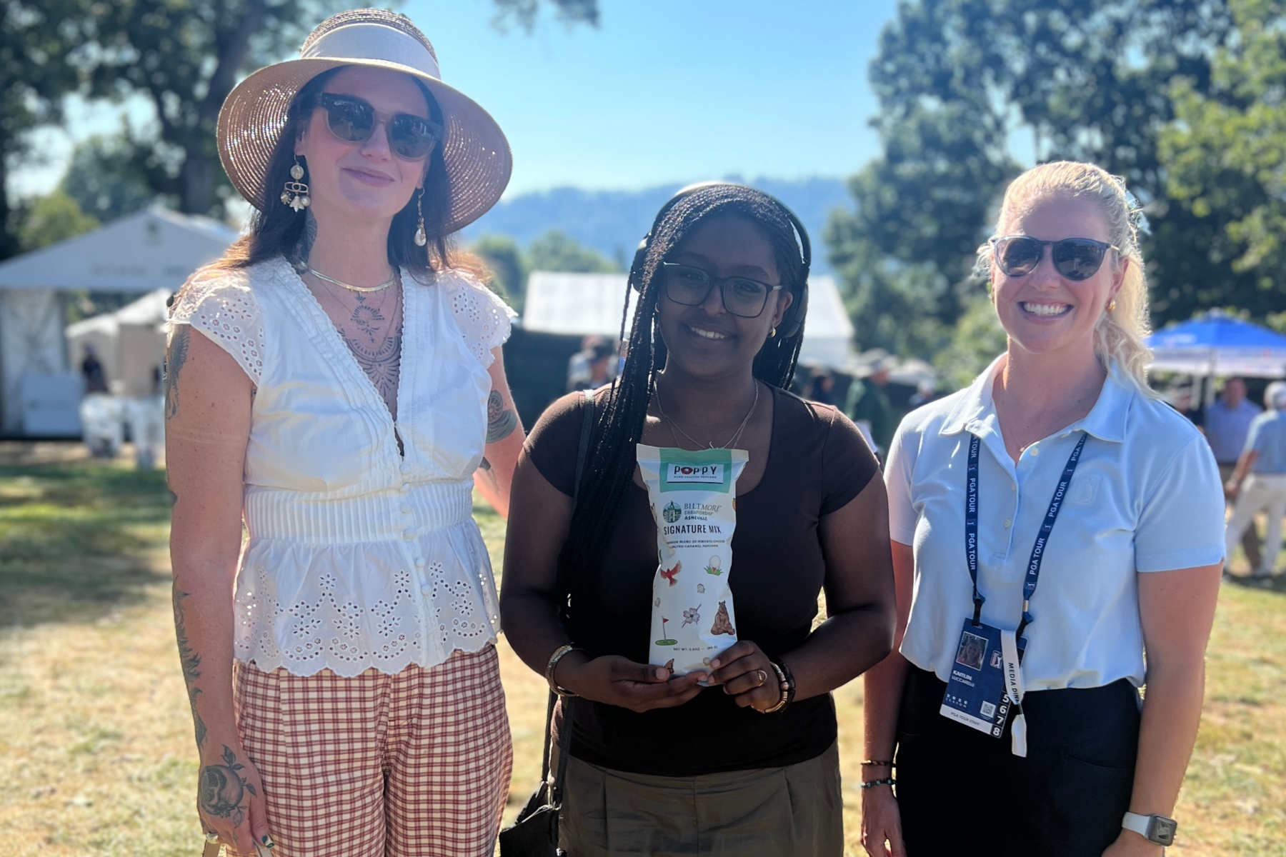 Asheville High School art teacher Kristina Shriver, left, and student Nia Teshome pose with a PGA TOUR representative during the Biltmore Championship Asheville. Teshome holds one of the limited-edition Poppy Hand-Crafted Popcorn bags featuring artwork created by Asheville High students.