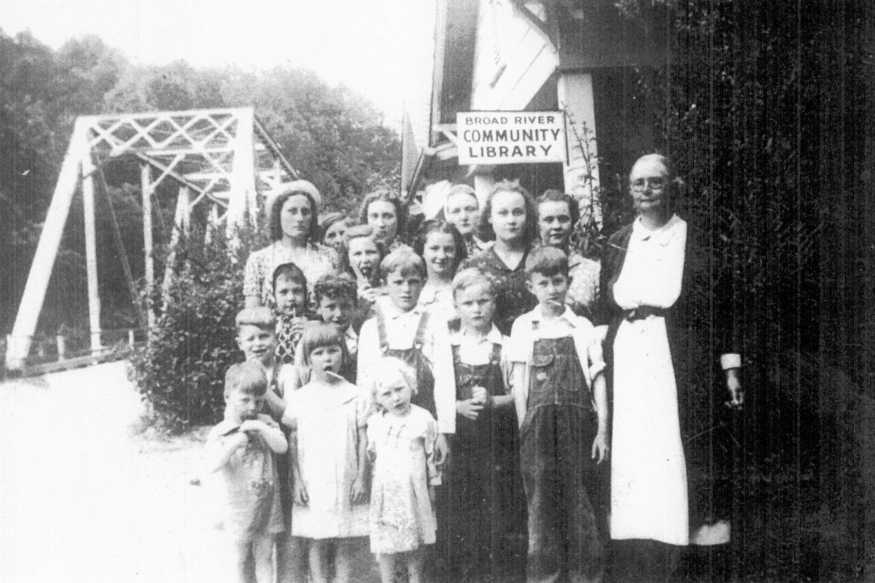 Nora Mae “Aunt Mae” Gilliam stands with children outside the tiny Broad River Community Library, which she operated in rural Buncombe County beginning in 1938. The 12-by-12-foot log building served residents with books and other reading materials.
