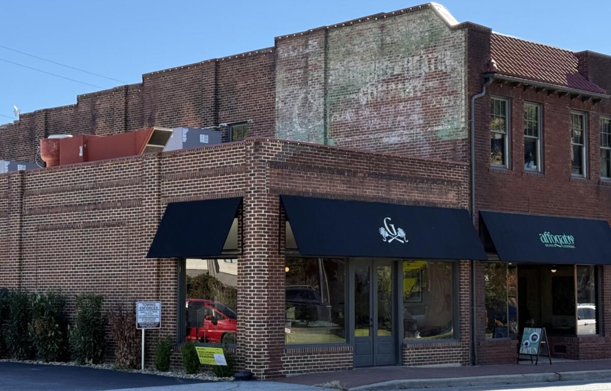A faded advertisement remains visible high on the brick wall of the former Biltmore Hardware building at 28-32 Hendersonville Road in Asheville's Biltmore Village. The old painted sign is a reminder of the building's commercial past, even as new businesses occupy the storefronts below.