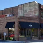 A faded advertisement remains visible high on the brick wall of the former Biltmore Hardware building at 28-32 Hendersonville Road in Asheville's Biltmore Village. The old painted sign is a reminder of the building's commercial past, even as new businesses occupy the storefronts below.