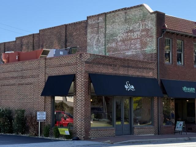 A faded advertisement remains visible high on the brick wall of the former Biltmore Hardware building at 28-32 Hendersonville Road in Asheville's Biltmore Village. The old painted sign is a reminder of the building's commercial past, even as new businesses occupy the storefronts below.