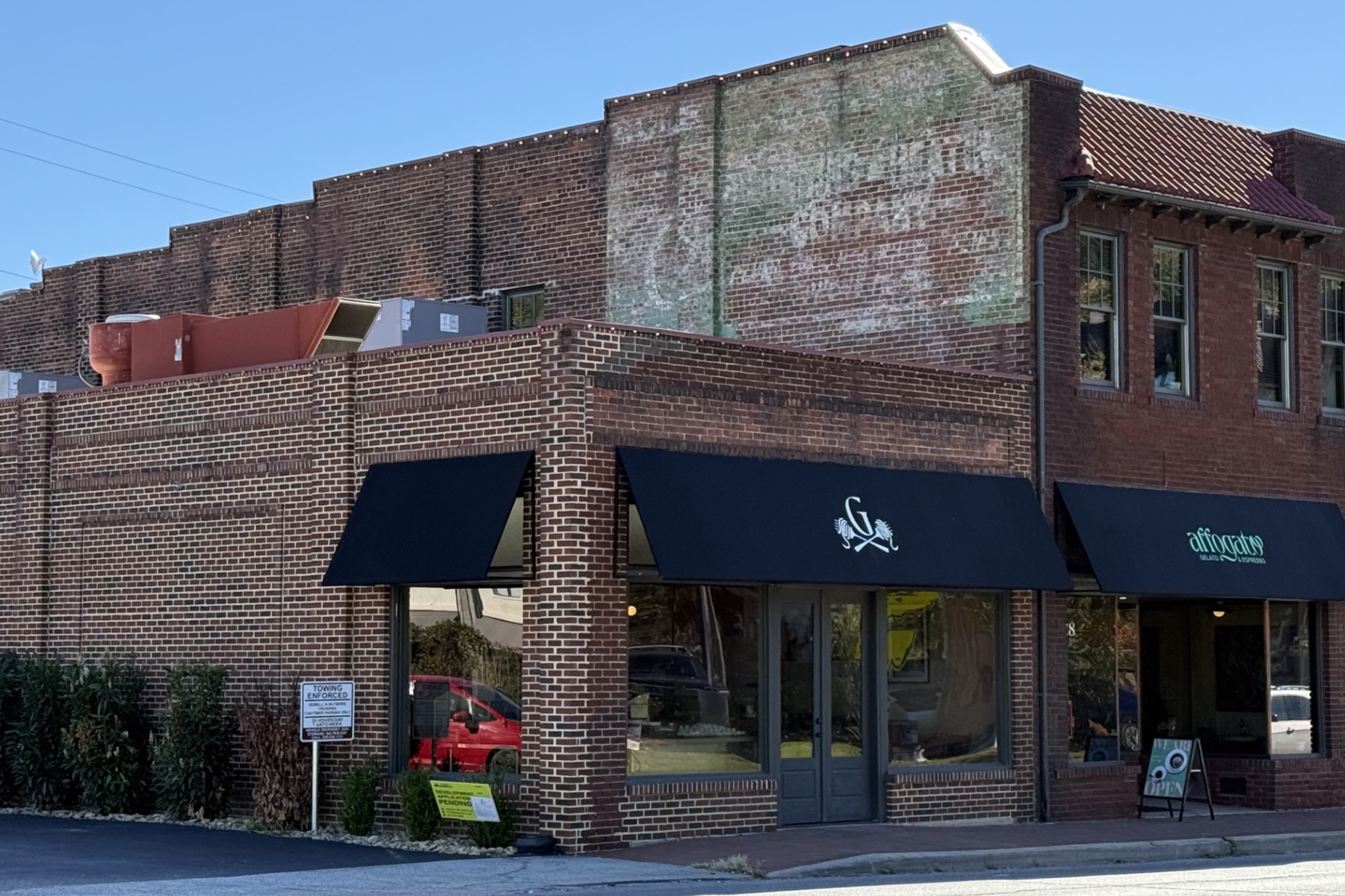 A faded advertisement remains visible high on the brick wall of the former Biltmore Hardware building at 28-32 Hendersonville Road in Asheville's Biltmore Village. The old painted sign is a reminder of the building's commercial past, even as new businesses occupy the storefronts below.