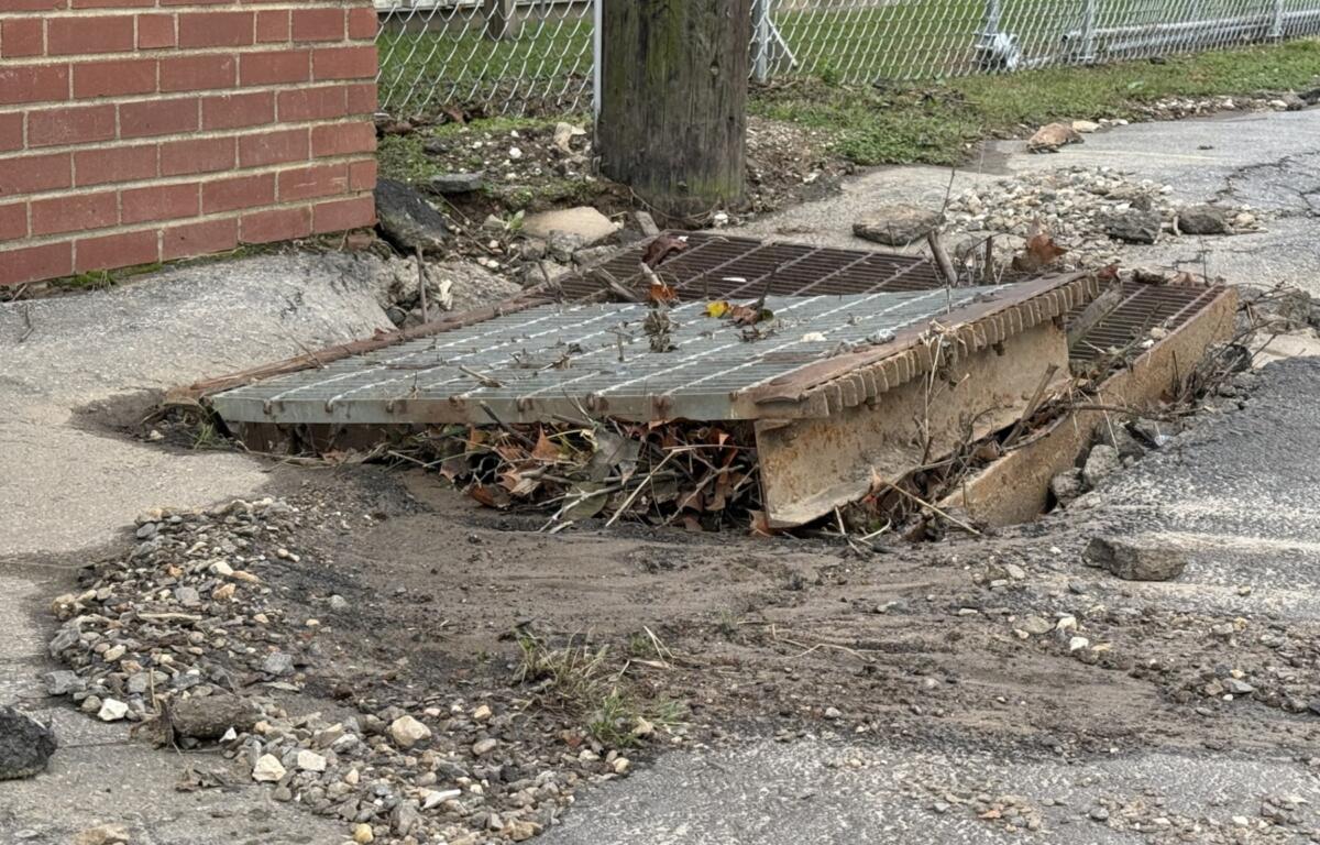 A displaced storm drain grate sits amid gravel, mud and debris along North Avenue in Swannanoa on Monday, Oct. 12, 2026.