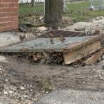 A displaced storm drain grate sits amid gravel, mud and debris along North Avenue in Swannanoa on Monday, Oct. 12, 2026.