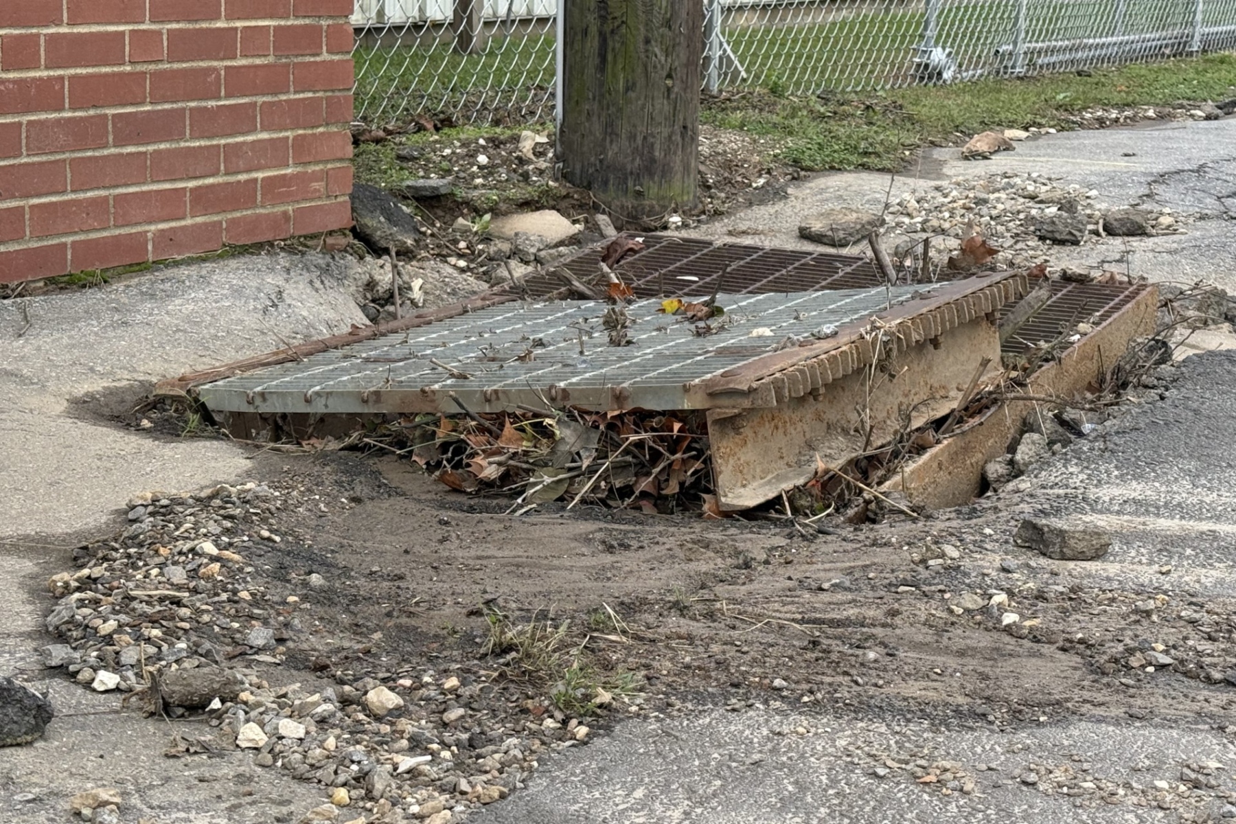A displaced storm drain grate sits amid gravel, mud and debris along North Avenue in Swannanoa on Monday, Oct. 12, 2026.