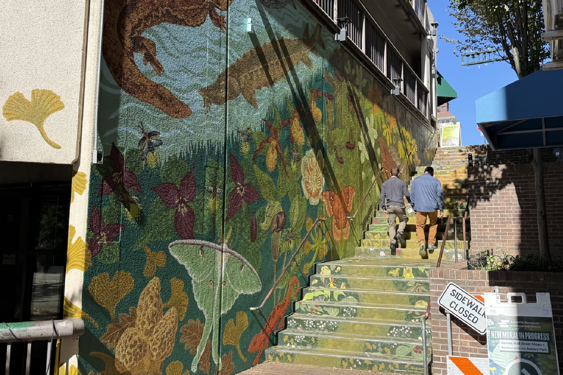 Two pedestrians walk up the colorful Wall Street steps in downtown Asheville, where artist Dayna Walton's "Meander" mural has been expanded onto the adjoining parking garage wall.