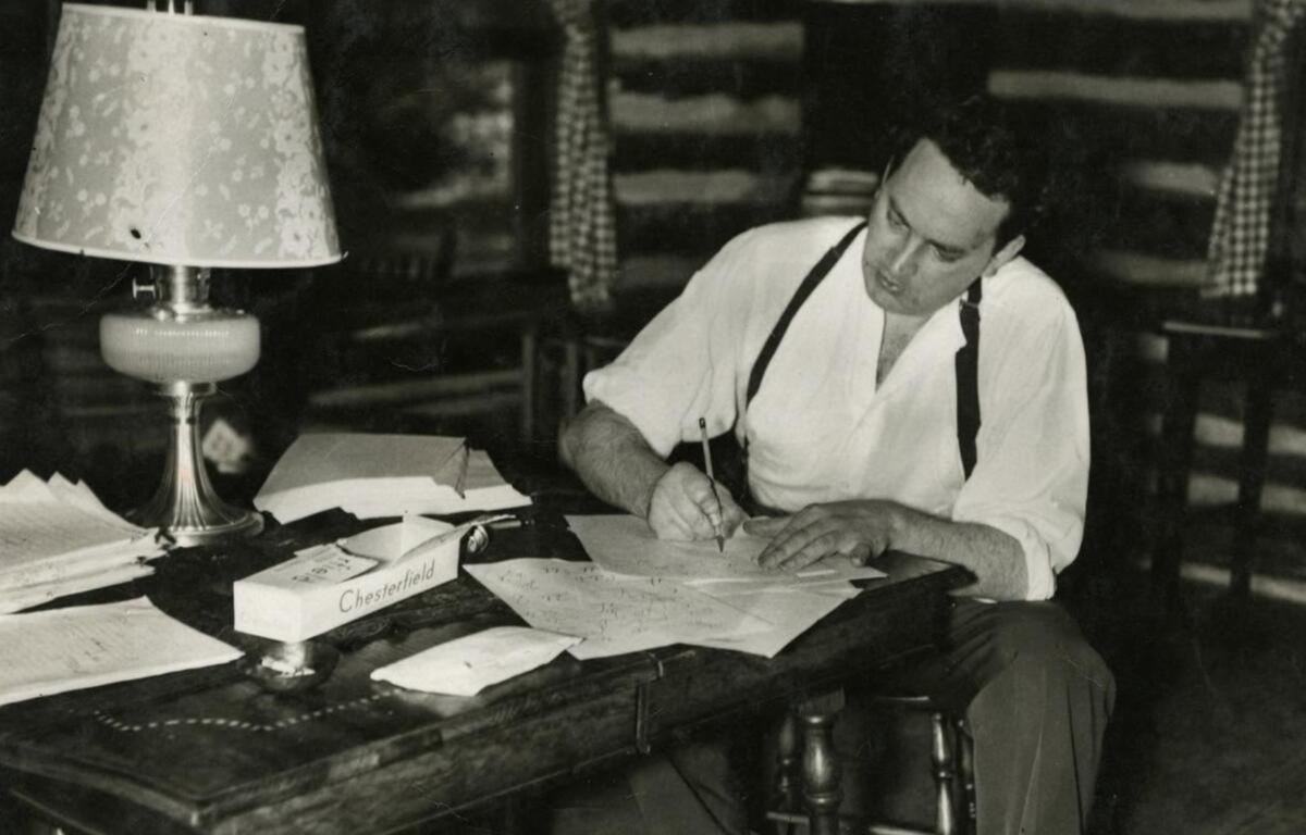Asheville native Thomas Wolfe works at a desk in a cabin in his hometown. Wolfe drew heavily on his childhood, family and Asheville experiences for his 1929 novel, "Look Homeward, Angel," in which he fictionalized the city as Altamont. (Public domain)