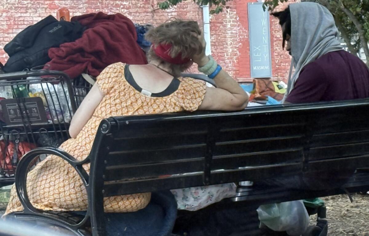 Two people who appear to be experiencing homelessness sit on a bench in Asheville. Concerns about homelessness and public safety in West Asheville have drawn increased attention from residents and city leaders.