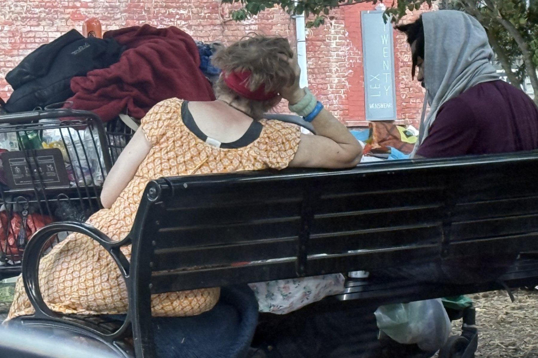 Two people who appear to be experiencing homelessness sit on a bench in Asheville. Concerns about homelessness and public safety in West Asheville have drawn increased attention from residents and city leaders.